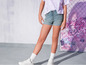 Une fille porte un short en jean bleu, un t-shirt blanc et des baskets blanches.