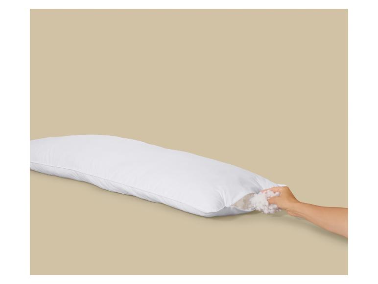 Oreiller rectangulaire blanc avec fermeture éclair ouverte et une main ajoutant du rembourrage.