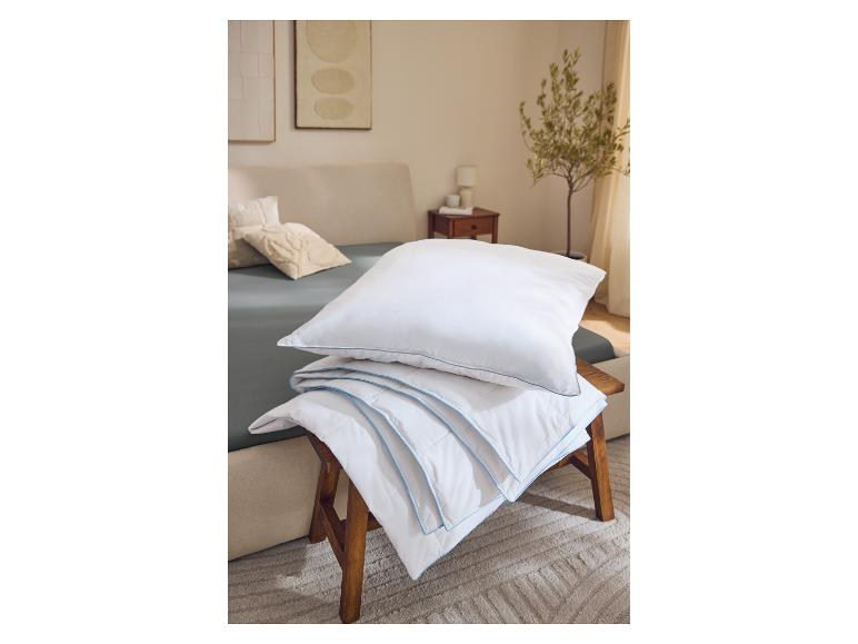 Oreillers et couette blancs avec liseré bleu sur un tabouret en bois dans une chambre.