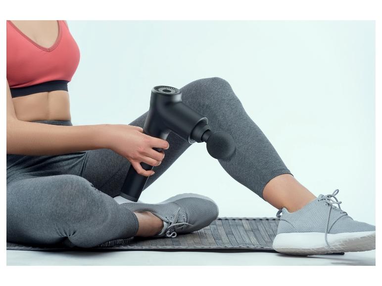 Une femme utilise un pistolet de massage sur sa jambe.