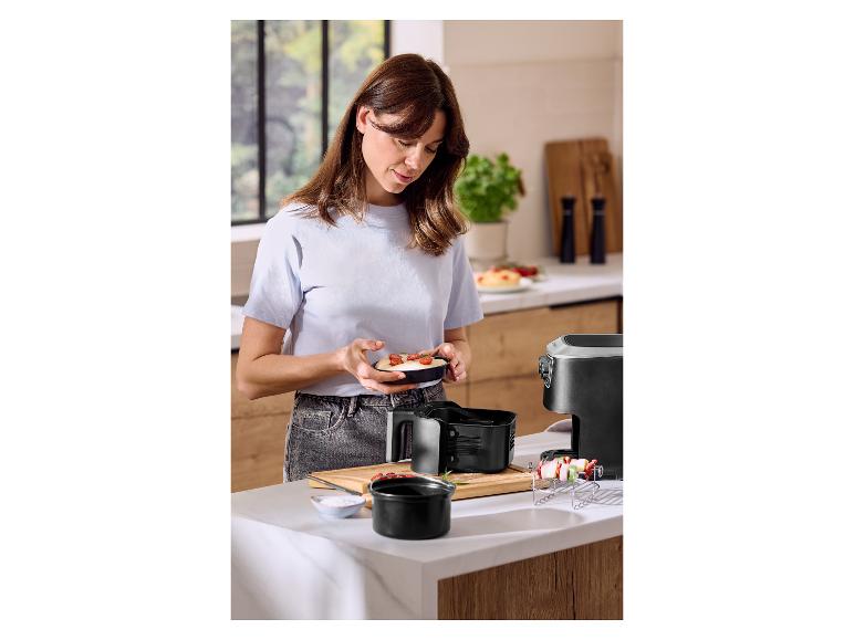 Femme préparant un repas dans la cuisine, tenant un petit plat, à côté d'une friteuse à air.