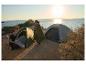 Couple campant au bord de la mer avec des tentes et un sac de couchage CRIVIT au coucher du soleil.