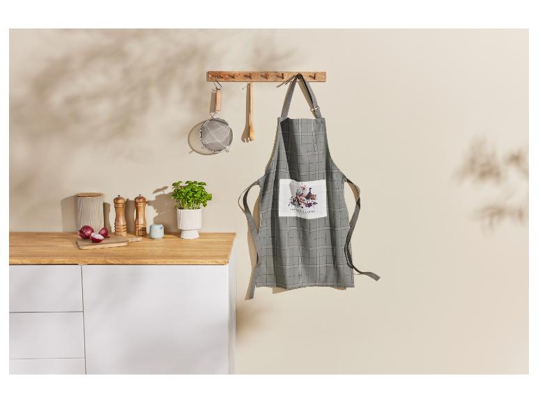 Un tablier de cuisine à carreaux avec un motif de jardin accroché à un support mural.