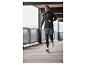 Homme en tenue de sport noire et short vert courant dans un garage.