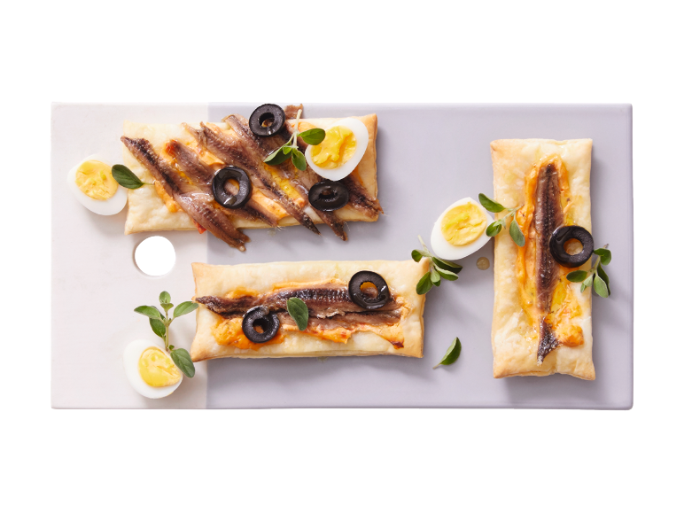 Feuilletés aux anchois, olives noires et œufs durs sur un plateau.