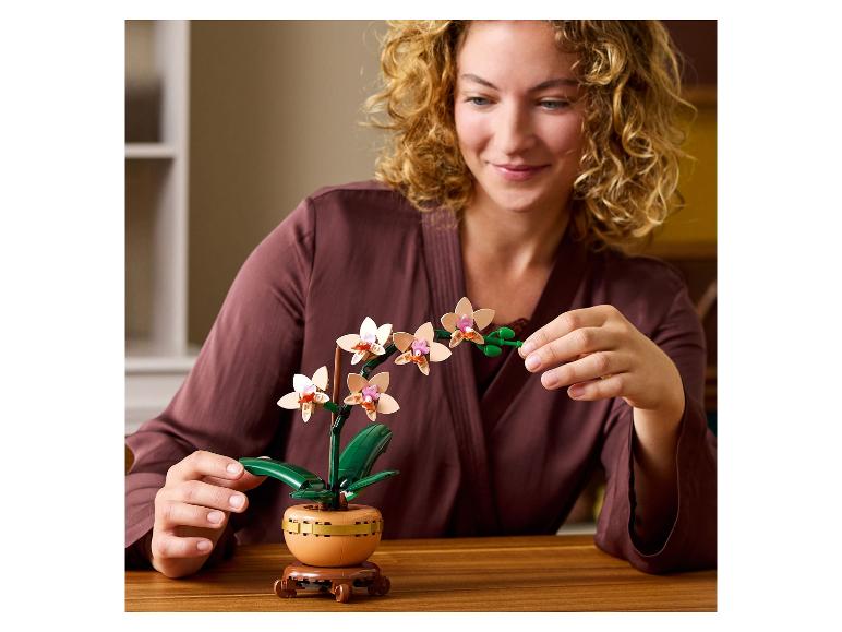 Femme souriante avec une orchidée à construire sur une table en bois.