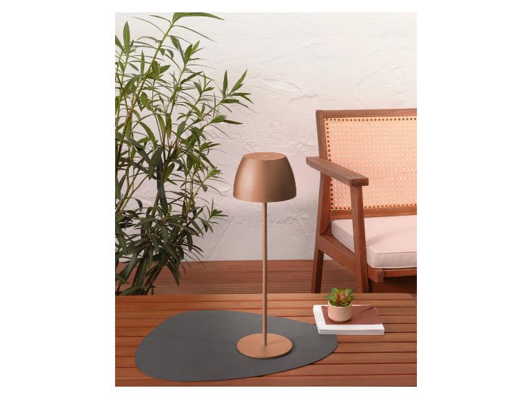 Une lampe de table moderne en bronze sur une table en bois avec une plante et une chaise.