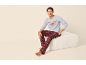 Homme assis sur un pouf, portant un sweat-shirt gris avec 'LETS STAY IN BED (FOREVER)' et un pantalon de pyjama écossais rouge.