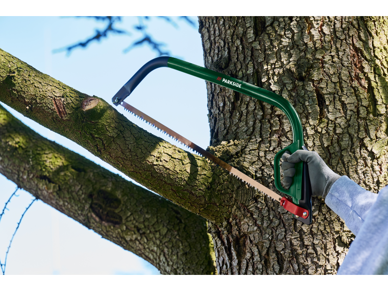 Scie de jardin avec un cadre vert et une poignée rouge coupant une branche d'arbre.