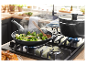 Des brocolis sont sautés dans une poêle et un plat mijote dans une casserole sur une cuisinière à gaz.