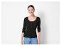 Une femme porte un t-shirt noir à manches longues avec des boutons et un jean bleu.