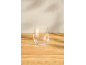 Verre sans pied transparent sur une table en bois clair avec des ombres murales subtiles.