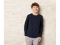 Un jeune homme portant un pull bleu marine et un pantalon gris.