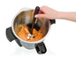Une main utilisant une spatule pour remuer de la purée dans un robot culinaire.