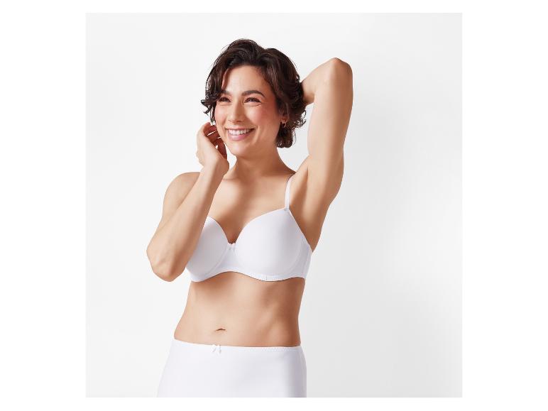 Une femme sourit en portant un soutien-gorge blanc et des sous-vêtements taille haute.