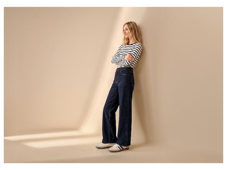 Femme en marinière et jean large, adossée à un mur, portant des baskets.