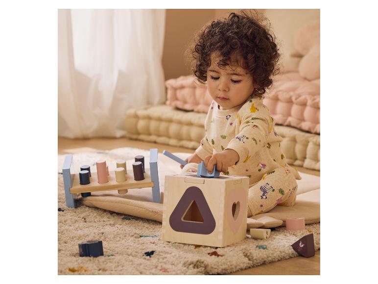 Un bébé joue avec une boîte à formes en bois et un banc à marteler sur un tapis.