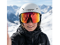 Personne avec casque de ski blanc et lunettes réfléchissantes, veste de ski noire, montagnes enneigées en arrière-plan.
