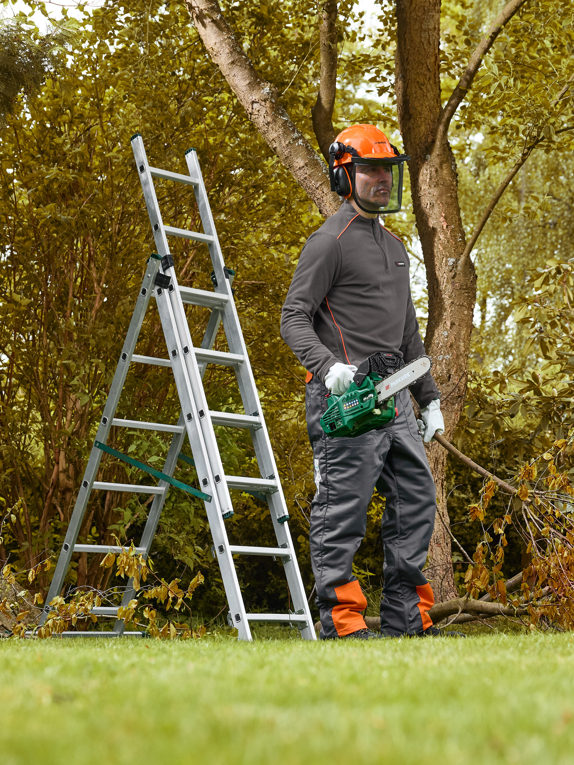 Homme avec casque de sécurité et tronçonneuse à côté d'une échelle, prêt à élaguer des arbres.
