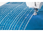 Machine à coudre réalisant des motifs décoratifs sur un tissu bleu.
