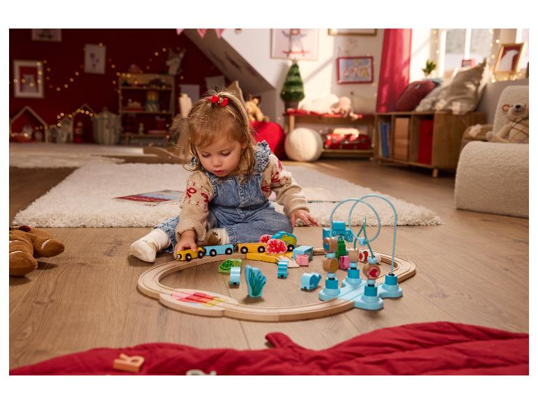 Enfant en bas âge jouant avec un train jouet en bois et d'autres jouets en bois colorés sur un tapis.