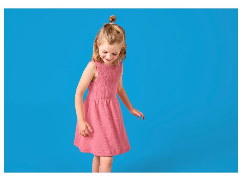 Petite fille en robe rose avec un chignon, regardant vers le bas.