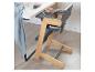 Chaise haute en bois et grise avec bol et cuillère sur le plateau, à côté d'une table.