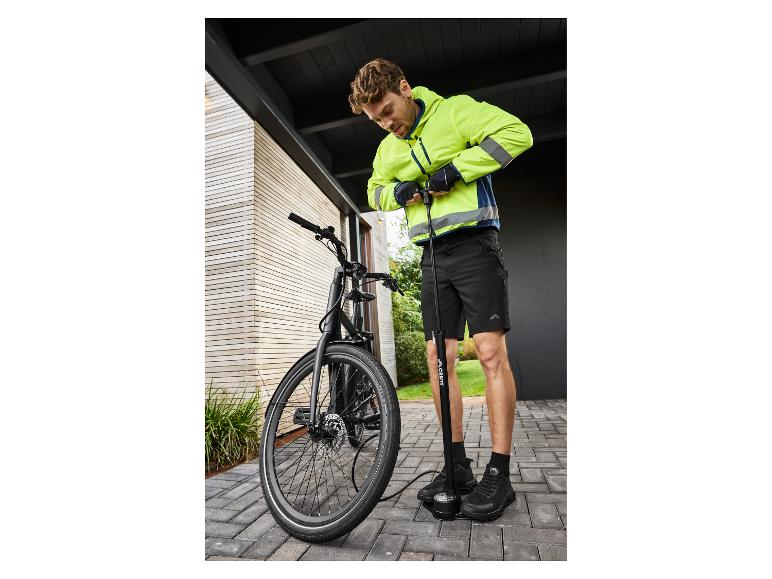 Homme en veste jaune fluo et short noir gonflant un pneu de vélo avec une pompe à pied.