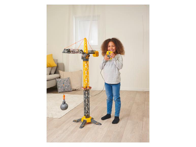 Une fille joue avec une grande grue jouet jaune avec une boule de démolition.