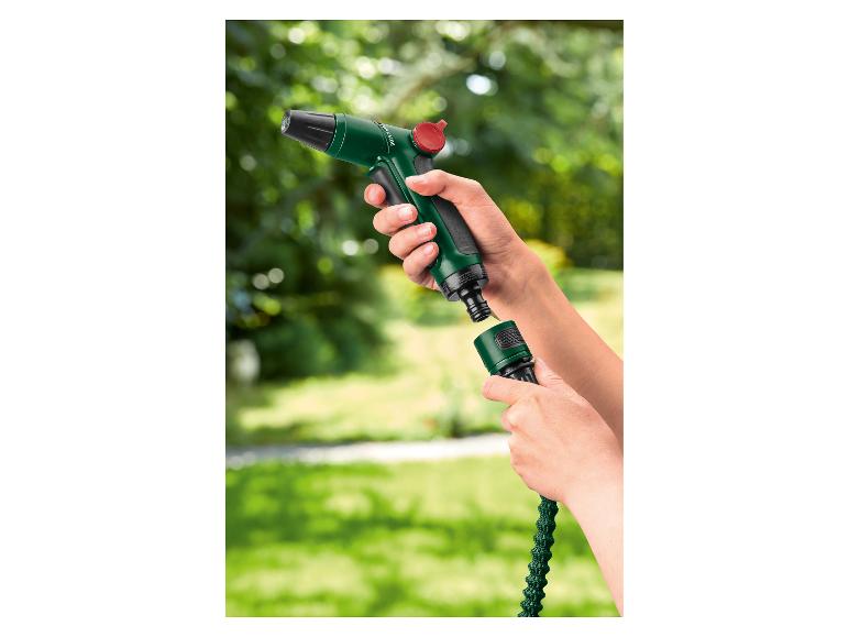 Mains connectant un pistolet d'arrosage vert à un tuyau d'arrosage extensible dans un jardin.
