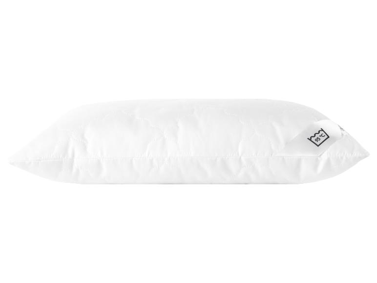 Oreiller blanc avec des détails matelassés et une étiquette avec instructions de lavage à 95°C.