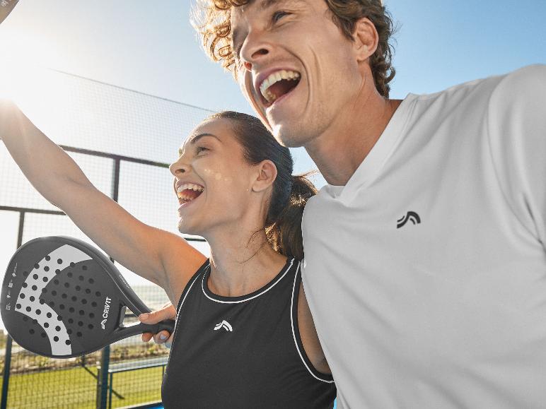 Deux personnes heureuses en tenue de sport, l'une tenant une raquette de padel, sur un court ensoleillé.