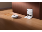 Robot aspirateur blanc avec station de charge nettoyant un sol en bois.
