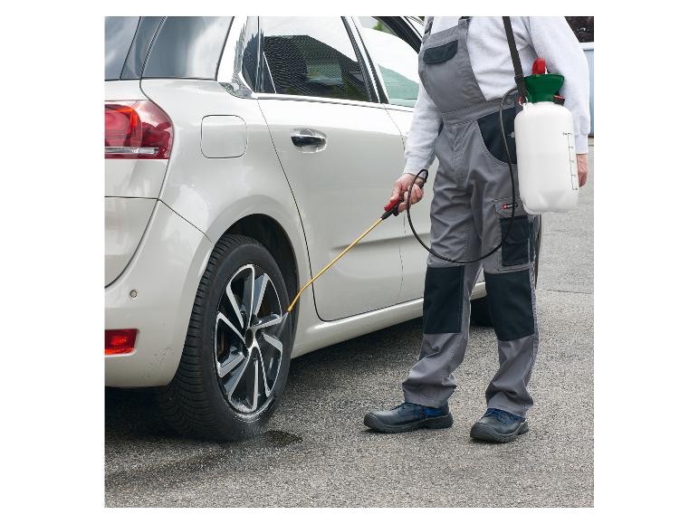 Homme en salopette nettoyant des pneus de voiture avec un pulvérisateur à pression.
