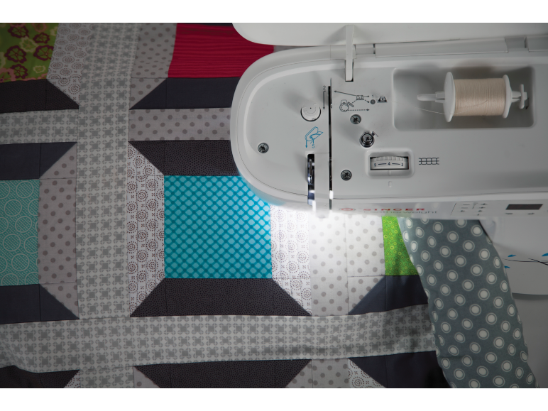 Machine à coudre avec une courtepointe aux motifs géométriques de couleurs et textures variées.