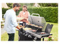 Un couple cuisine des hamburgers, des saucisses et du maïs sur un barbecue à gaz noir.