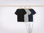 Trois t-shirts, un noir, un gris et un bleu marine, accrochés à un cintre en bois.