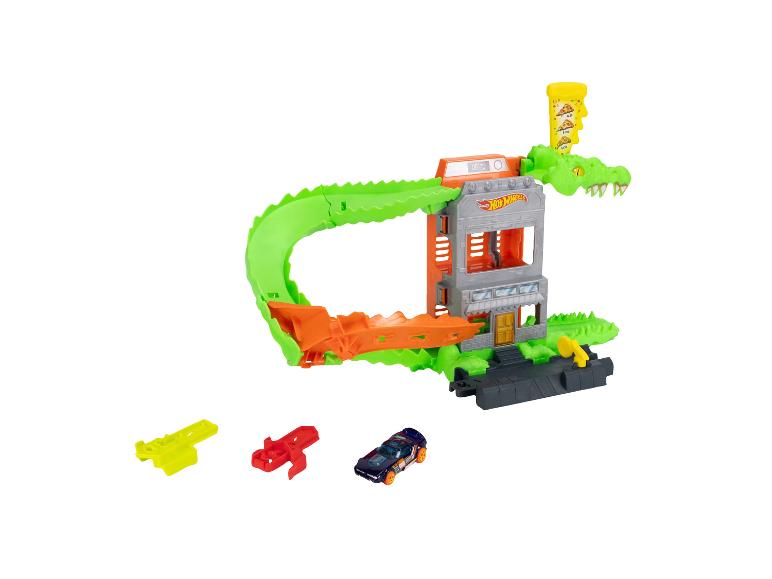 Circuit de voitures jouets avec un alligator vert, un bâtiment et une voiture jouet bleu foncé.