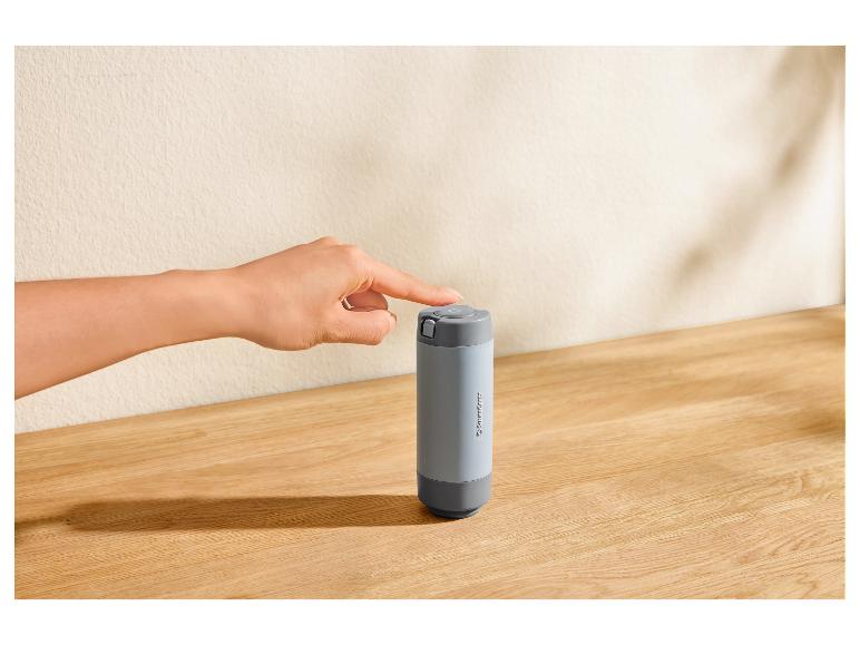 Main appuyant sur un bouton d'un thermos gris SilverCrest sur un comptoir en bois.