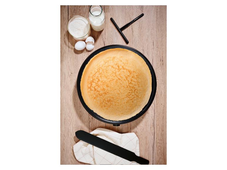 Vue de dessus d'une crêpière avec une crêpe dorée, entourée de farine, de lait et d'œufs.