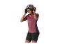 Femme en maillot de cyclisme bordeaux et short noir, ajustant son casque gris.