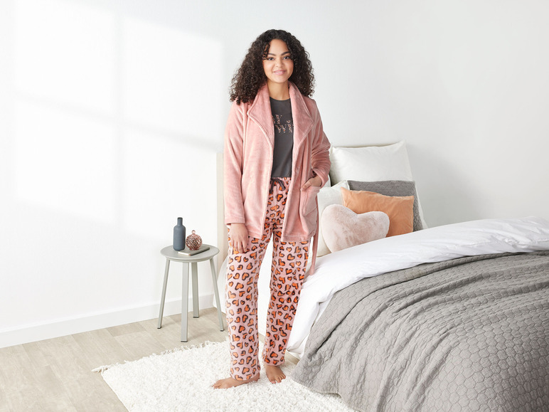 Une femme en pyjama rose à motif cœur et robe de chambre rose.