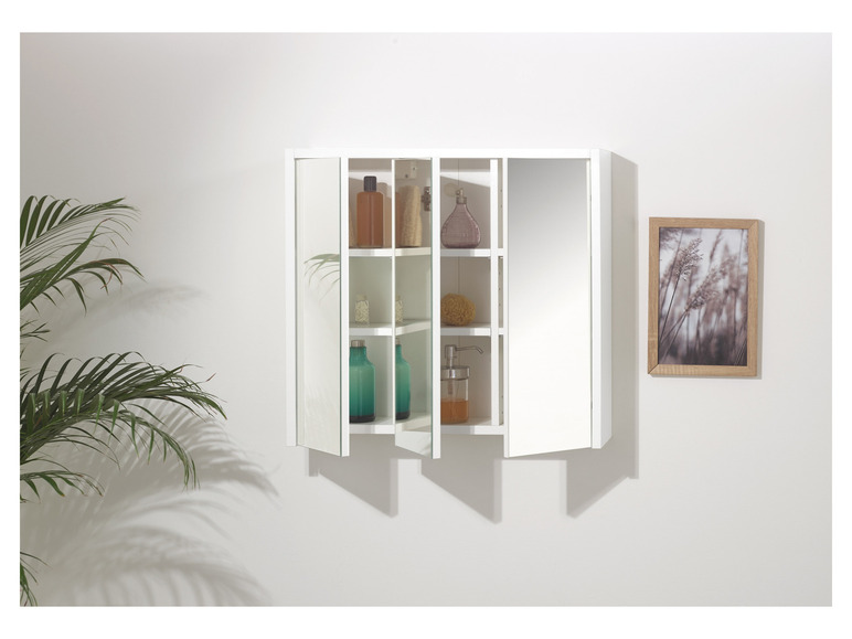 Une armoire de salle de bain blanche avec des portes en miroir, ouverte avec des bouteilles et un distributeur.