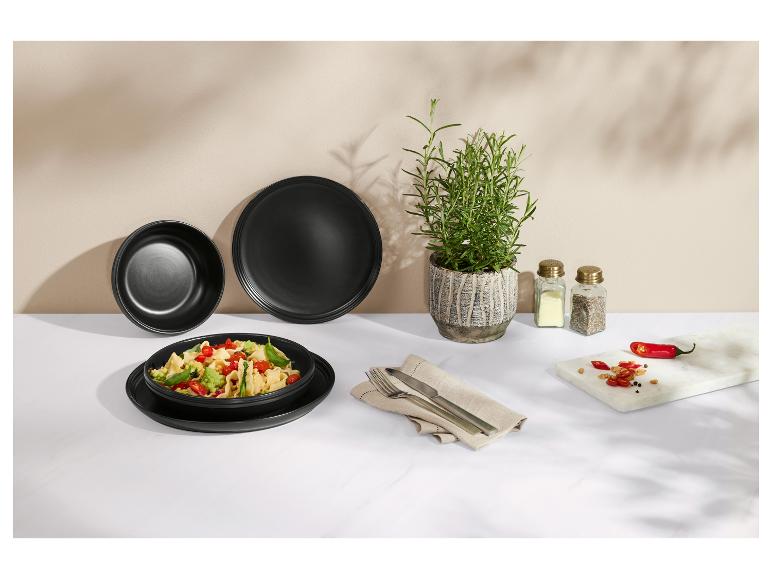 Assiettes noires avec pâtes, romarin, sel et poivre, piments sur planche de marbre.