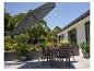 Ensemble de salle à manger d'extérieur avec parasol sur une terrasse, vue sur jardin et maison.