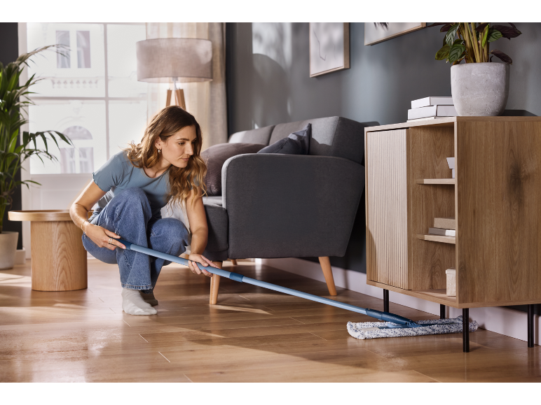 Femme nettoyant un sol en bois avec une serpillière plate dans un salon moderne.
