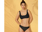 Une femme en bikini noir devant un fond jaune.