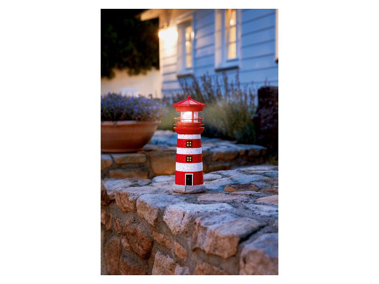 Une lampe solaire en forme de phare rouge et blanc dans un jardin