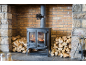 Poêle à bois avec ventilateur sur le conduit de cheminée, entouré de bois de chauffage empilé.