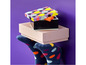 Une boîte LEGO à points colorés, sur une boîte rose, tenue par deux chaussettes à motifs amusants.